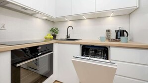 A modern kitchen with white cabinetry, a black dishwasher, and a built-in oven. - Functional Apartment | Parking, Workspace (Warszawa)