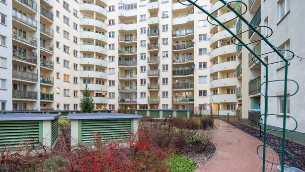A multi-story residential building with balconies, a brick pathway, and green railings. - Functional Apartment | Parking, Workspace (Warszawa)