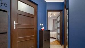 A hallway with a wooden door, a small cabinet, and a bed in the background. - Functional Apartment | Parking, Workspace (Warszawa)