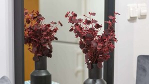 A dining area with a black table, two dark vases with red flowers, a plate, and a mirror reflecting the room. - Functional Apartment | Parking, Workspace (Warszawa)