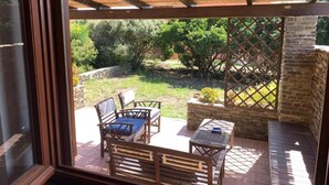 Un porche cubierto con mobiliario de madera y vistas al jardín.