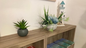Una consola de madera con una planta en maceta, un cuenco decorativo con flores y una pequeña maqueta de faro. Abajo, hay libros y revistas.