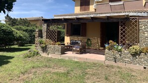 Una casa de dos pisos con un patio, muros de piedra y un área de estar cubierta.