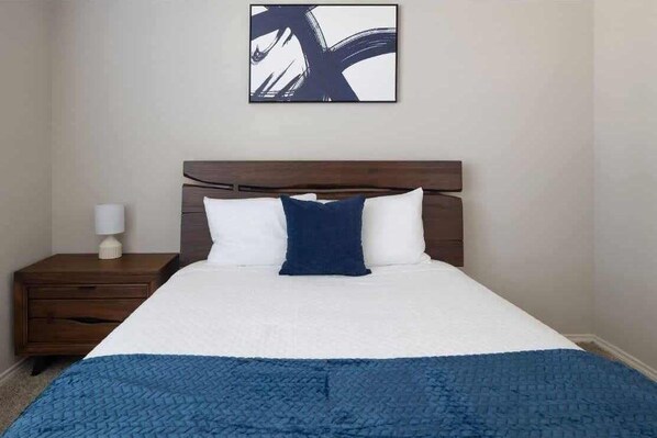 Habitación de hotel con una cama, una mesita de noche, una lámpara y una obra de arte abstracta colgada en la pared.