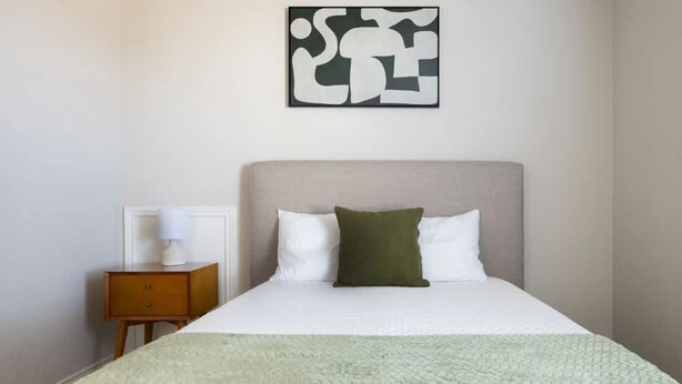 Habitació d'hotel amb llit, una tauleta de nit, una làmpada i una obra d'art a la paret.