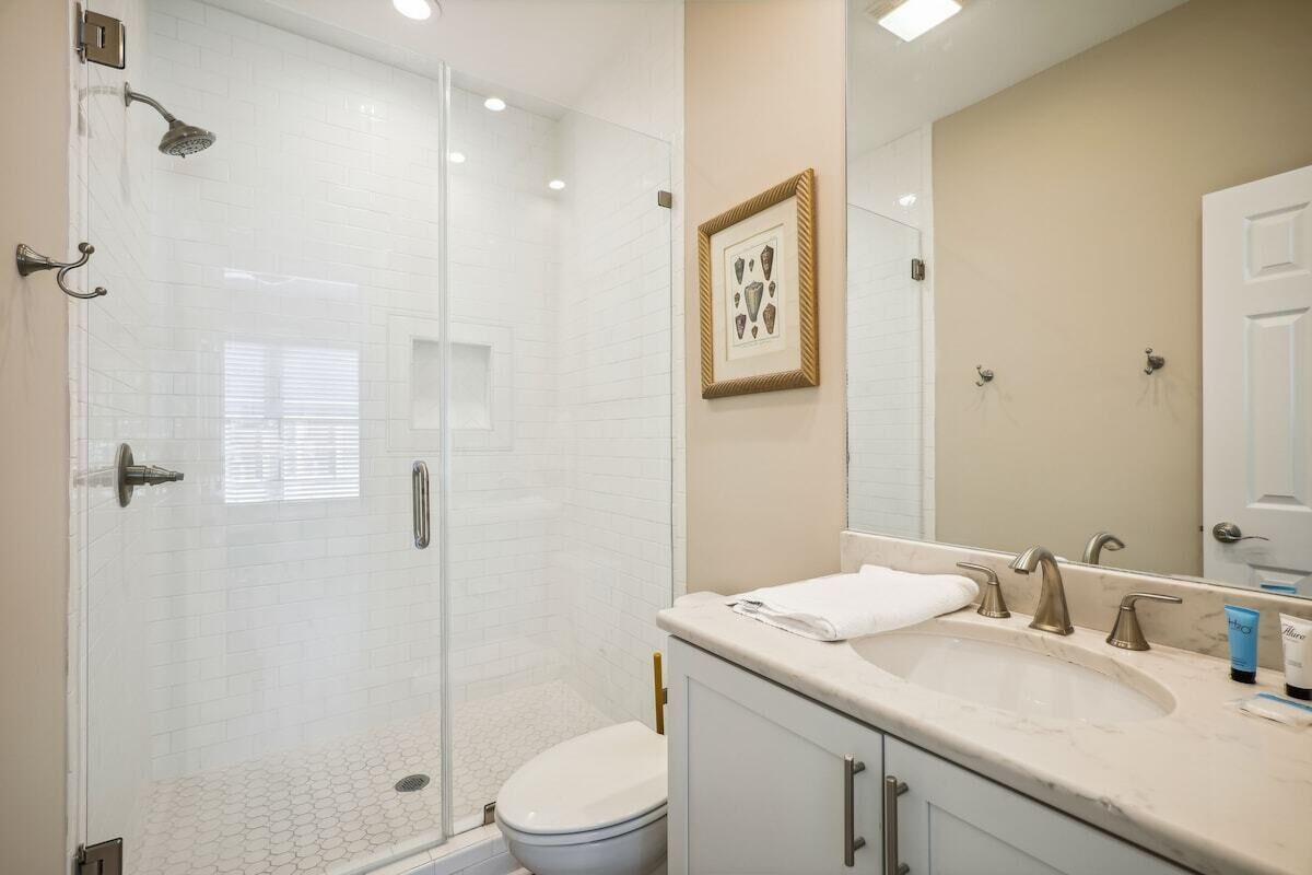 Une salle de bain moderne avec une douche à parois de verre, des toilettes blanches, un meuble-lavabo et un grand miroir.