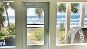 A room with a view of the ocean through a door and window, a covered grill outside, and potted plants inside.