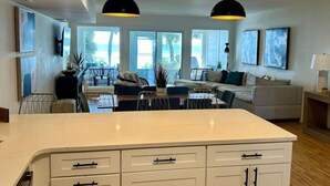 A modern kitchen with a large island, dining area with chairs, and a sofa.