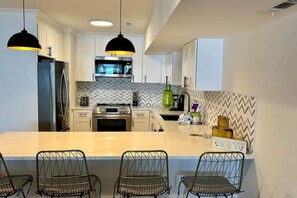 Una cocina moderna con armarios blancos, un refrigerador de acero inoxidable, un horno empotrado y una isla central con taburetes de bar.