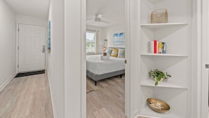 Un couloir menant à une chambre à coucher, où se trouvent un lit, une bibliothèque et une porte.