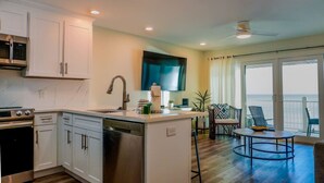 A modern kitchen with white cabinets, a built-in oven, and a dishwasher. There is a dining area with a round table and chairs, and a large window offering a view of the ocean. - Seamist 7 ~ Beachfront on 30A (Seacrest)