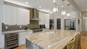 Une cuisine moderne avec des armoires blanches, un grand îlot central, des appareils en acier inoxydable et des luminaires suspendus.
