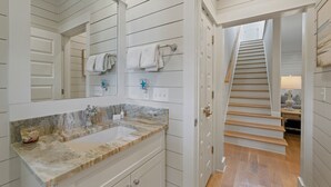 Une salle de bain avec un lavabo en marbre, un grand miroir et un escalier menant à l’étage supérieur.