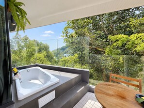 A modern bathroom with a large bathtub, a glass shower enclosure, and a view of lush greenery.