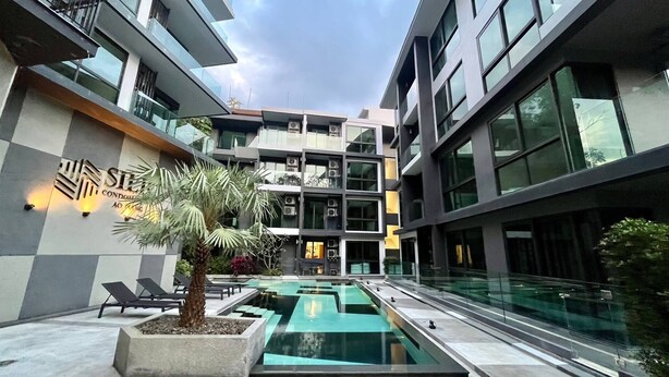 A modern building with a swimming pool, lounge chairs, and a sign for 'STELLA CONDOMINIUM'.