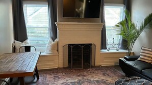 Una sala de estar con chimenea, ventilador de techo, televisor de pantalla plana, mesa de comedor y sofá.