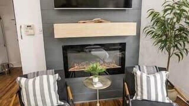 A modern living room with a flat-screen TV mounted on the wall, a fireplace below, two striped armchairs, a small round table, and a potted plant. - Spacious Corporate Lodging in Downtown Lafayette (Lafayette)