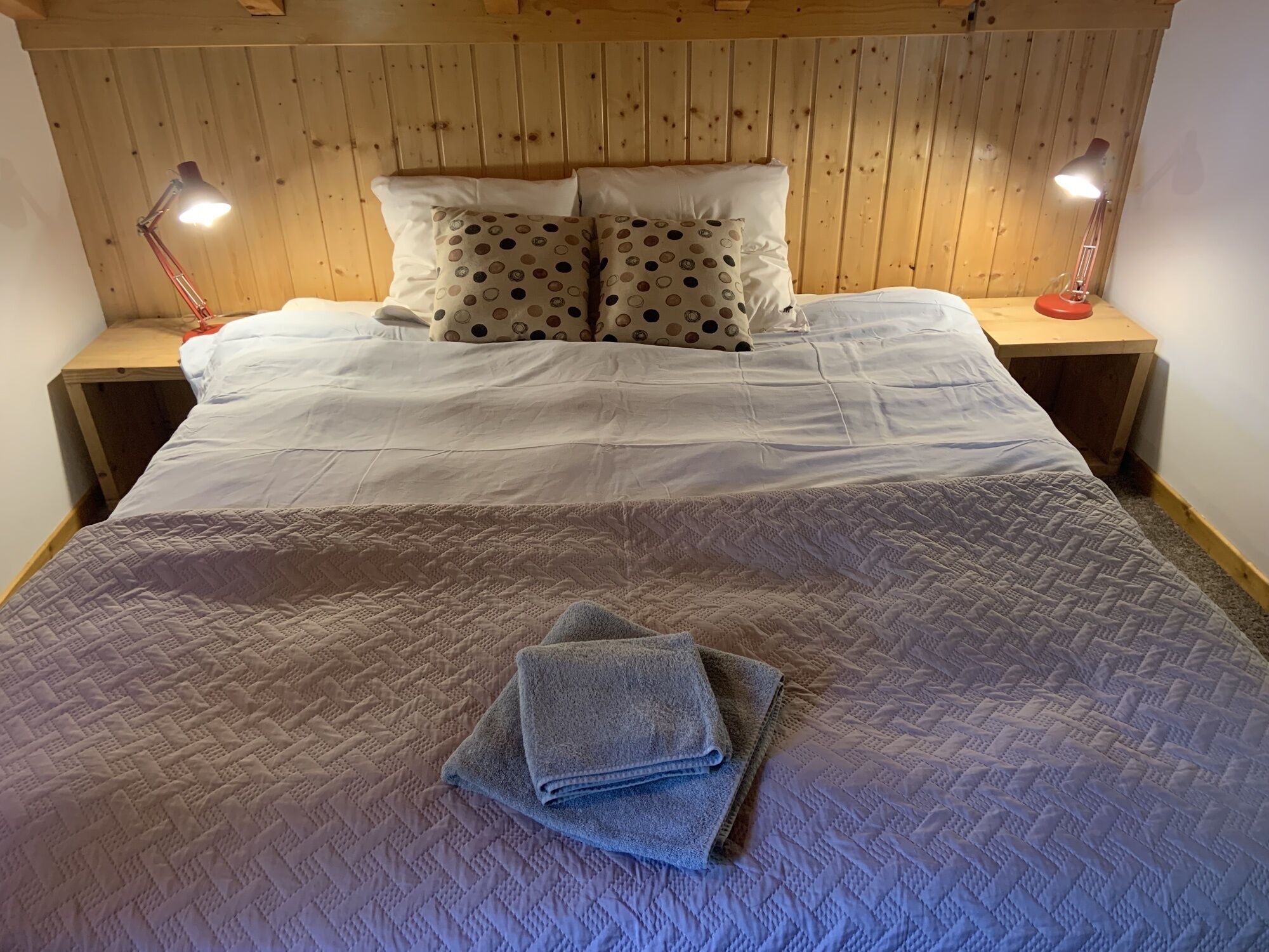 A neatly made bed with a quilt, two pillows with a polka dot pattern, and two bedside lamps on wooden nightstands.