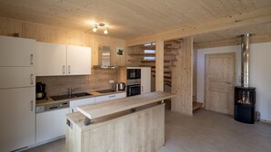 A modern kitchen with wooden cabinetry, a central island, stainless steel appliances, and a wood-burning stove. - Murau 11 - large terrace & good location (Murau)