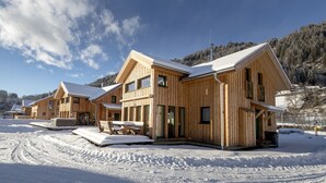 A wooden cabin complex with a snow-covered roof, a covered outdoor seating area, and a view of a forested mountain in the background. - Murau 11 - large terrace & good location (Murau)