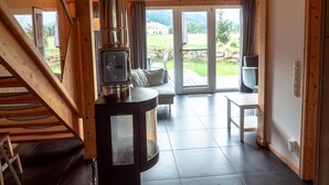 A wooden interior with a modern stove, a staircase, and a view of a green landscape through large glass doors. - Murau 9 - with infrared sauna and whirlpool (Murau)
