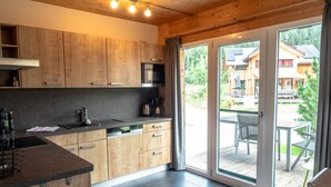 A modern kitchen with wooden cabinets, a black countertop, and a dishwasher. There is a sliding glass door leading to an outdoor patio with a table and chairs. - Murau 9 - with infrared sauna and whirlpool (Murau)