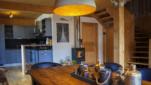 Una mesa de comedor de madera con una bandeja de botellas y vasos, techo de madera, cocina con armarios azules y una chimenea.