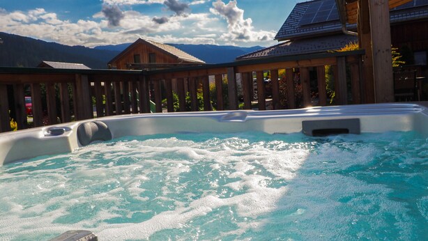Un jacuzzi con terraza de madera y montañas al fondo.