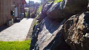 Un sendero que conduce a un edificio de madera, rodeado de grandes rocas y follaje.