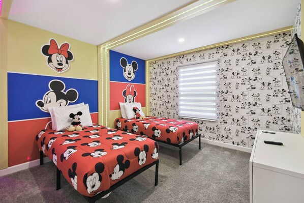 Une chambre pour enfants avec deux lits, chacun agrémenté de linge de lit sur le thème de Mickey Mouse, d’un autocollant mural à l’effigie de Mickey Mouse et d’un coussin à l’effigie de Mickey Mouse.