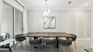 A modern dining area with a large wooden table, tufted chairs, and a contemporary light fixture.