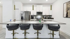 A modern kitchen with white cabinets, stainless steel appliances, a central island with bar stools, and pendant lighting.