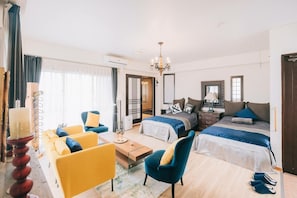A hotel room with two beds, a sofa, a chair, a small table, and a chandelier.