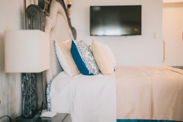 A neatly made bed with white bedding and patterned pillows, a bedside table with a lamp, and a flat-screen TV mounted on the wall. - RAINBOW SEA Maeda Hills (Onna)