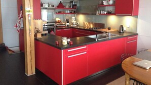 Een moderne keuken met rode kasten, roestvrijstalen apparatuur en een centraal kookeiland met spoelbak.