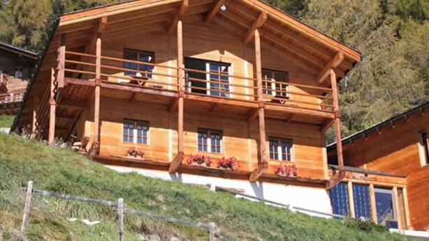 Een houten chalet met meerdere balkons, grote ramen en een schuin dak, omringd door bomen.