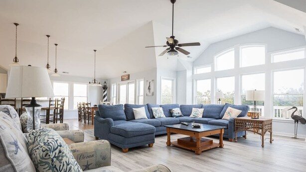 A spacious living room with a large sectional sofa, a coffee table, and a dining area with chairs and a table. - 2min Walk to Beach, Pool, Spa, Game Room, Big Yard (Corolla)