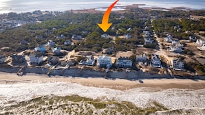An aerial view of a coastal residential area with houses, a beach, and a lighthouse in the distance. - 2min Walk to Beach, Pool, Spa, Game Room, Big Yard (Corolla)