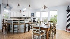 A spacious kitchen with white cabinets, a central island with bar stools, and pendant lighting. - 2min Walk to Beach, Pool, Spa, Game Room, Big Yard (Corolla)