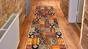 A hallway with a patterned rug, stone walls, a wooden ceiling, and a white door. - Arton In Cappadocia (Avanos)
