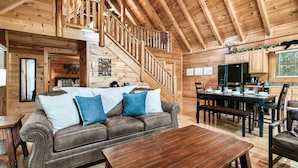 A wooden cabin interior with a sofa, dining table, and staircase. - Cozy Bear Heaven: Cuddle Up in the Smokies (Sevierville)