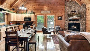 A spacious cabin interior with a stone fireplace, wooden ceiling, and a dining area. - Cozy Bear Heaven: Cuddle Up in the Smokies (Sevierville)