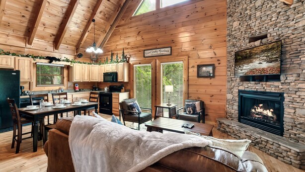 A cozy cabin interior with a stone fireplace, wooden ceiling beams, and a dining area. - Cozy Bear Heaven: Cuddle Up in the Smokies (Sevierville)