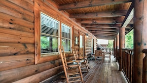 A wooden cabin with a porch featuring rocking chairs and a dining table. - Cozy Bear Heaven: Cuddle Up in the Smokies (Sevierville)