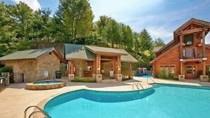 A pool area with a hot tub, wooden cabins, and a large building with a balcony.