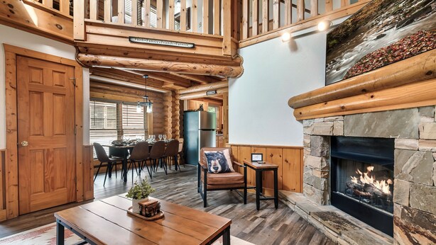 A cozy interior with a stone fireplace, wooden ceiling, and a dining area with chairs and a table.