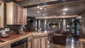 A rustic kitchen with wooden cabinets, a stone fireplace, and a cozy seating area with a leather couch. - Redwood in the Historic Upper Canyon (Ruidoso)