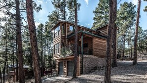 A two-story log cabin with a balcony, surrounded by tall pine trees. - Redwood in the Historic Upper Canyon (Ruidoso)