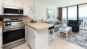 Eine moderne Küche mit integriertem Mikrowellenherd und Backofen, ein Essbereich mit kleinem Tisch und Stühlen sowie ein Balkon mit Meerblick.