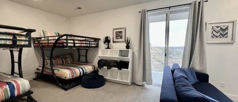 A room with bunk beds, a sofa, a fan, a window with curtains, and a view.